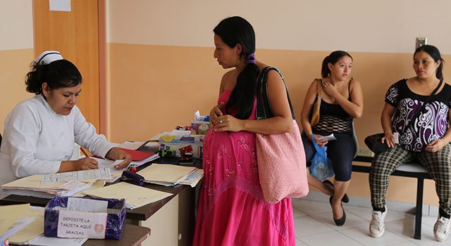 Image of a pregnant woman registering with a nurse sitting at a desk.