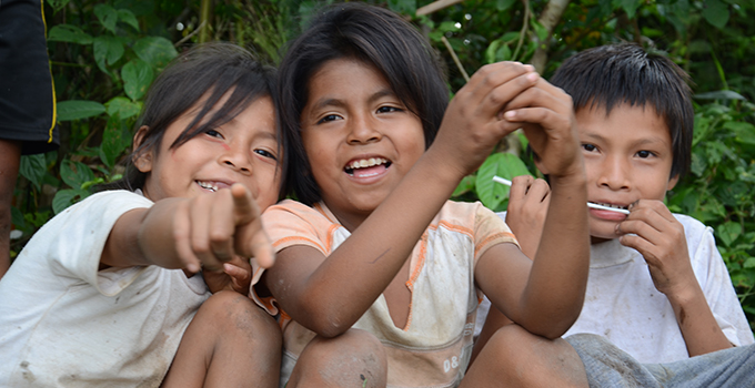 Photo of three children sitting outdoors and smiling.